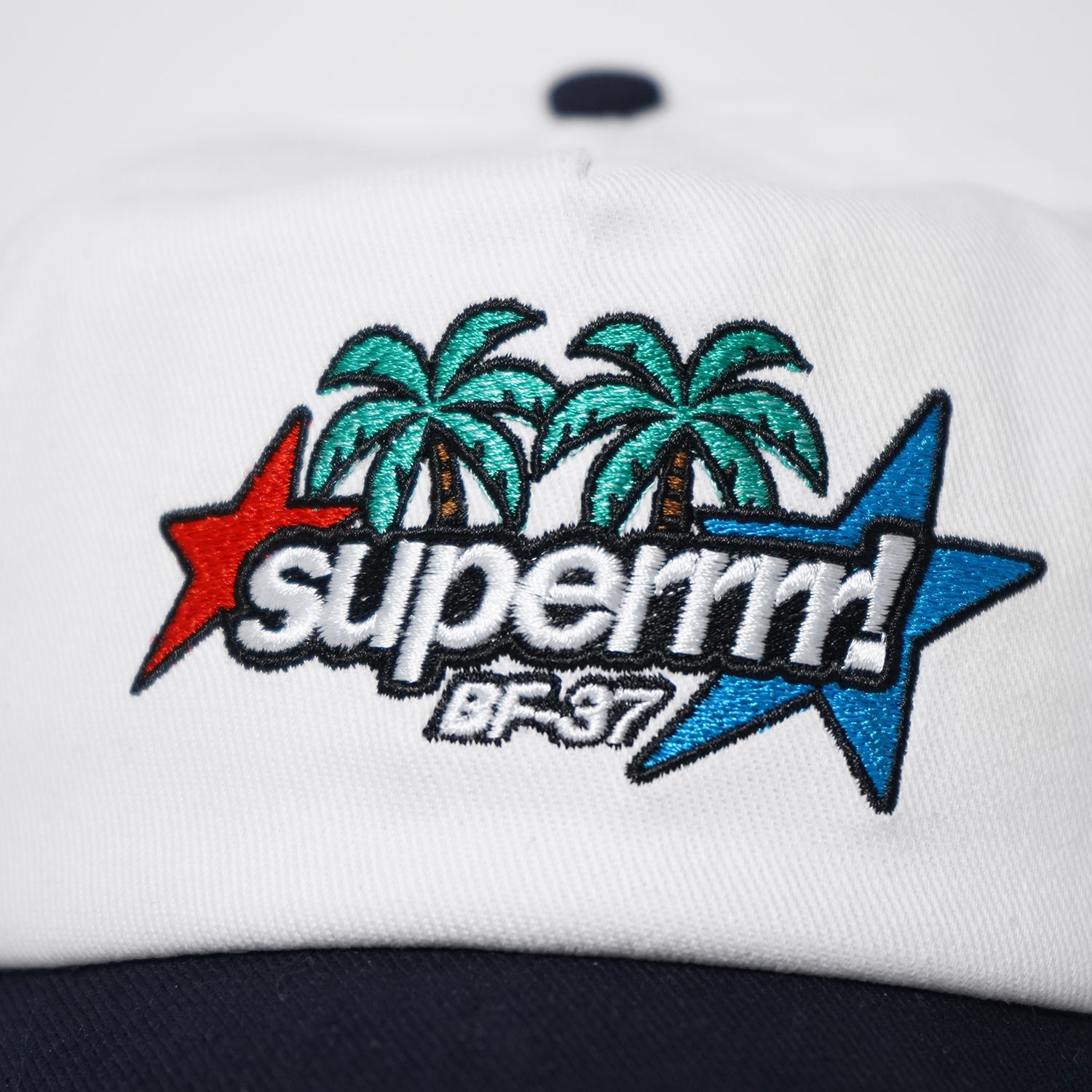 White cap with embroidered palm trees and 'superior' logo on a white background