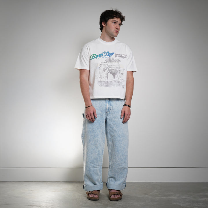 Person wearing a white t-shirt with graphic design and light blue jeans against a plain background