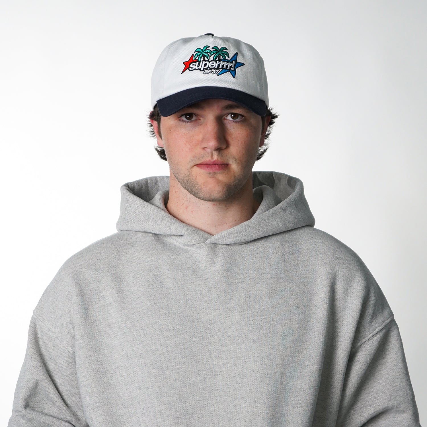 Man wearing a gray hoodie and a white cap with a colorful logo on a white background
