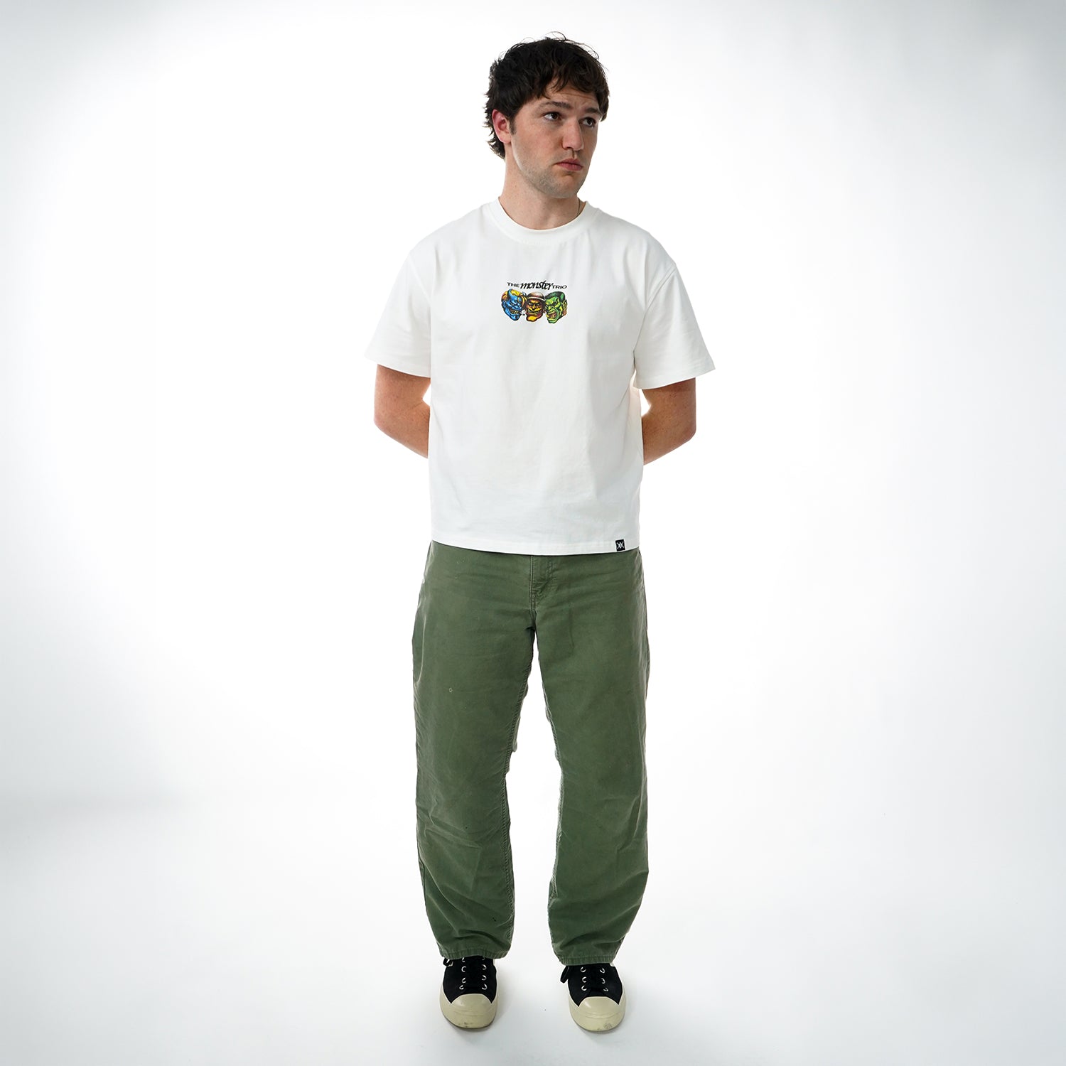 Man wearing a white t-shirt with a graphic design and green pants on a white background