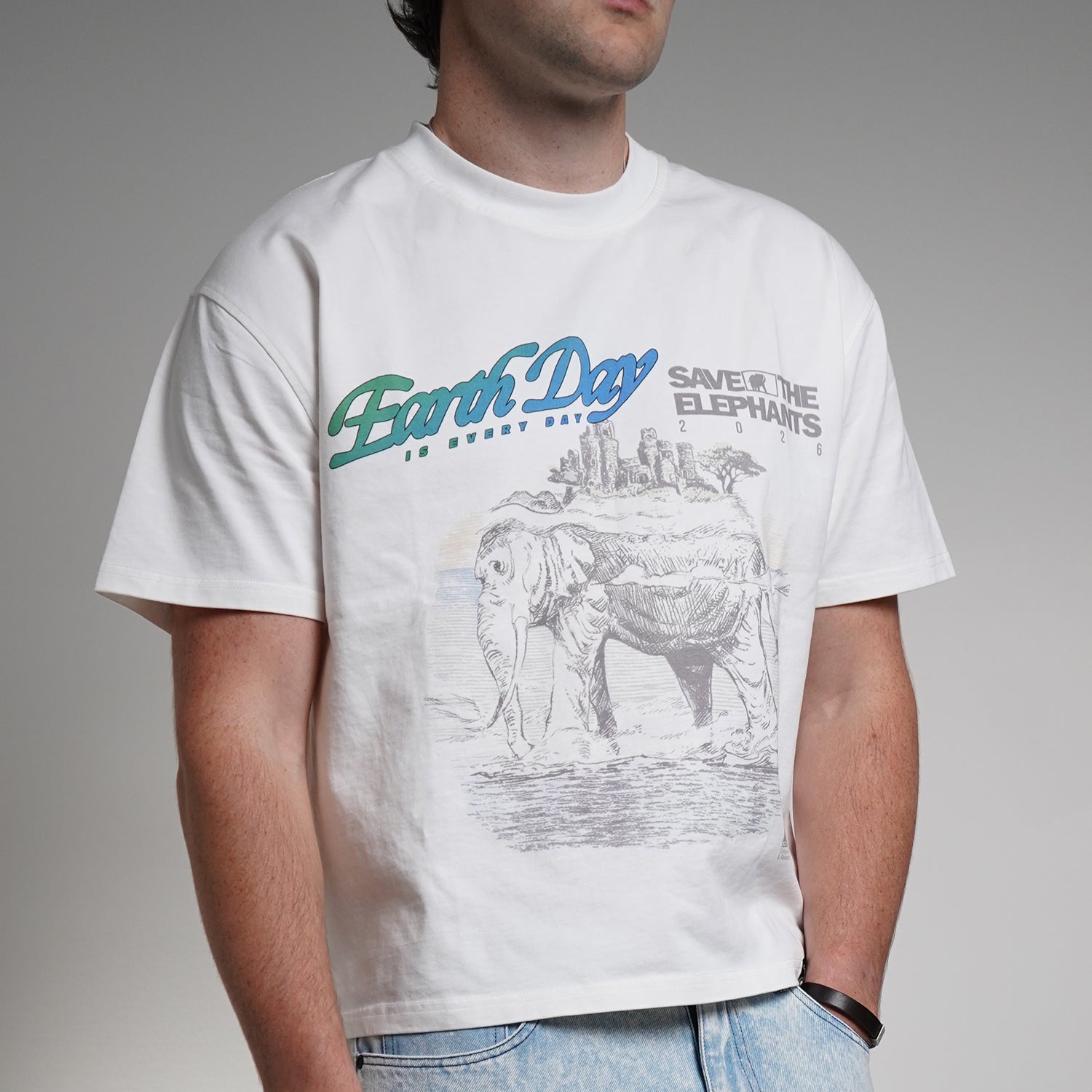 Person wearing a white t-shirt with 'Earth Day Save the Elephants' design on a gray background