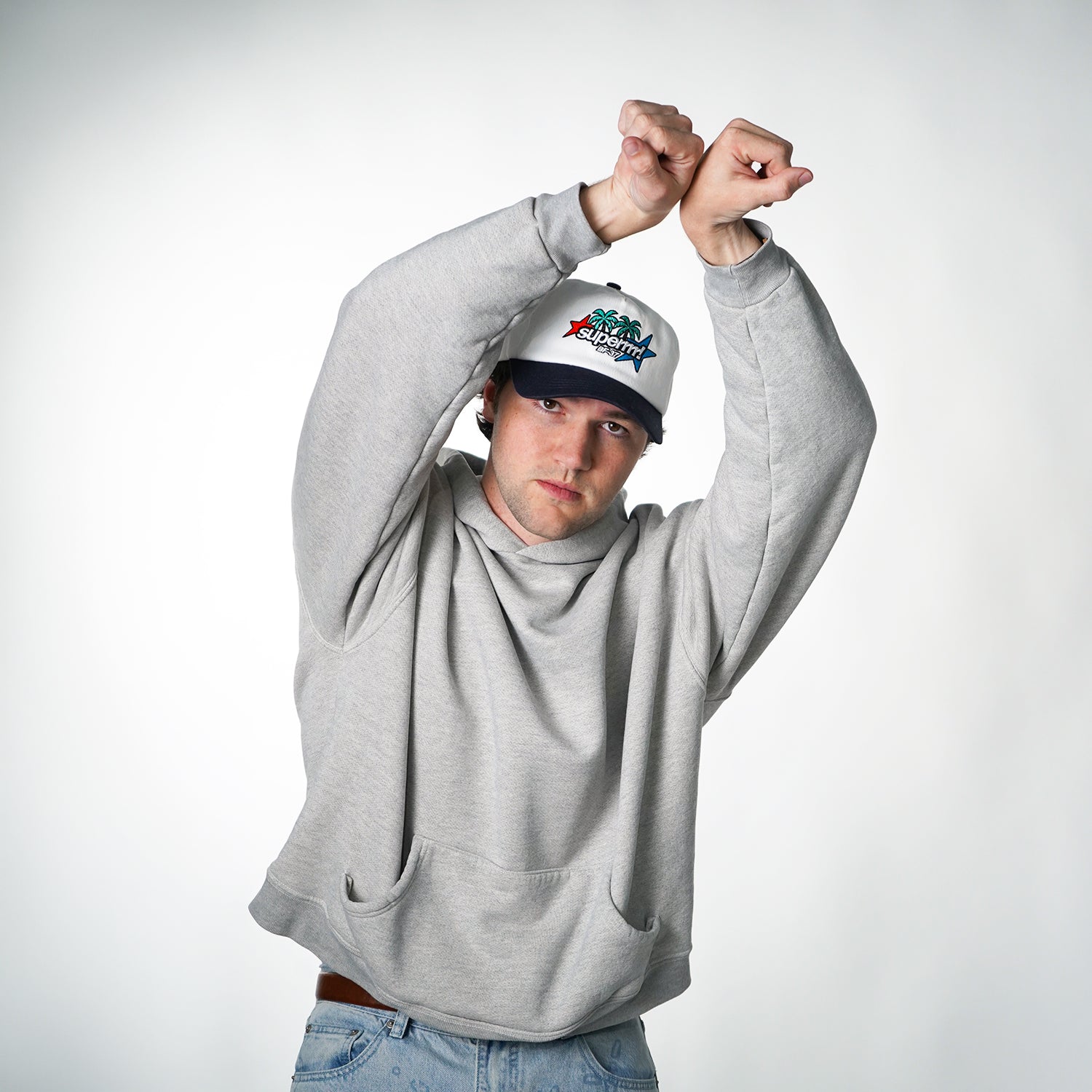 Person wearing a gray hoodie and a cap with a logo on a white background