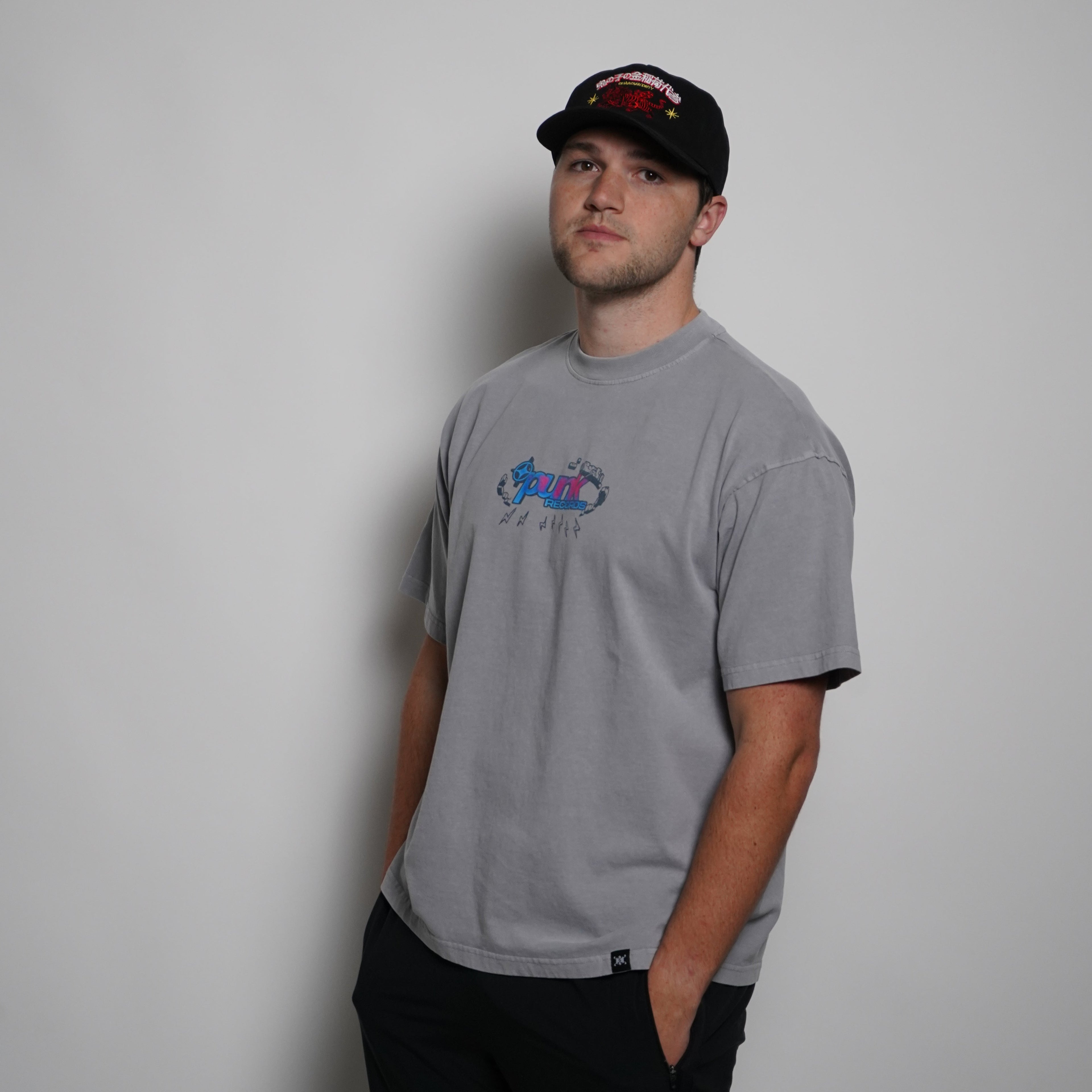 Person wearing a gray t-shirt with a logo and a black cap on a plain background