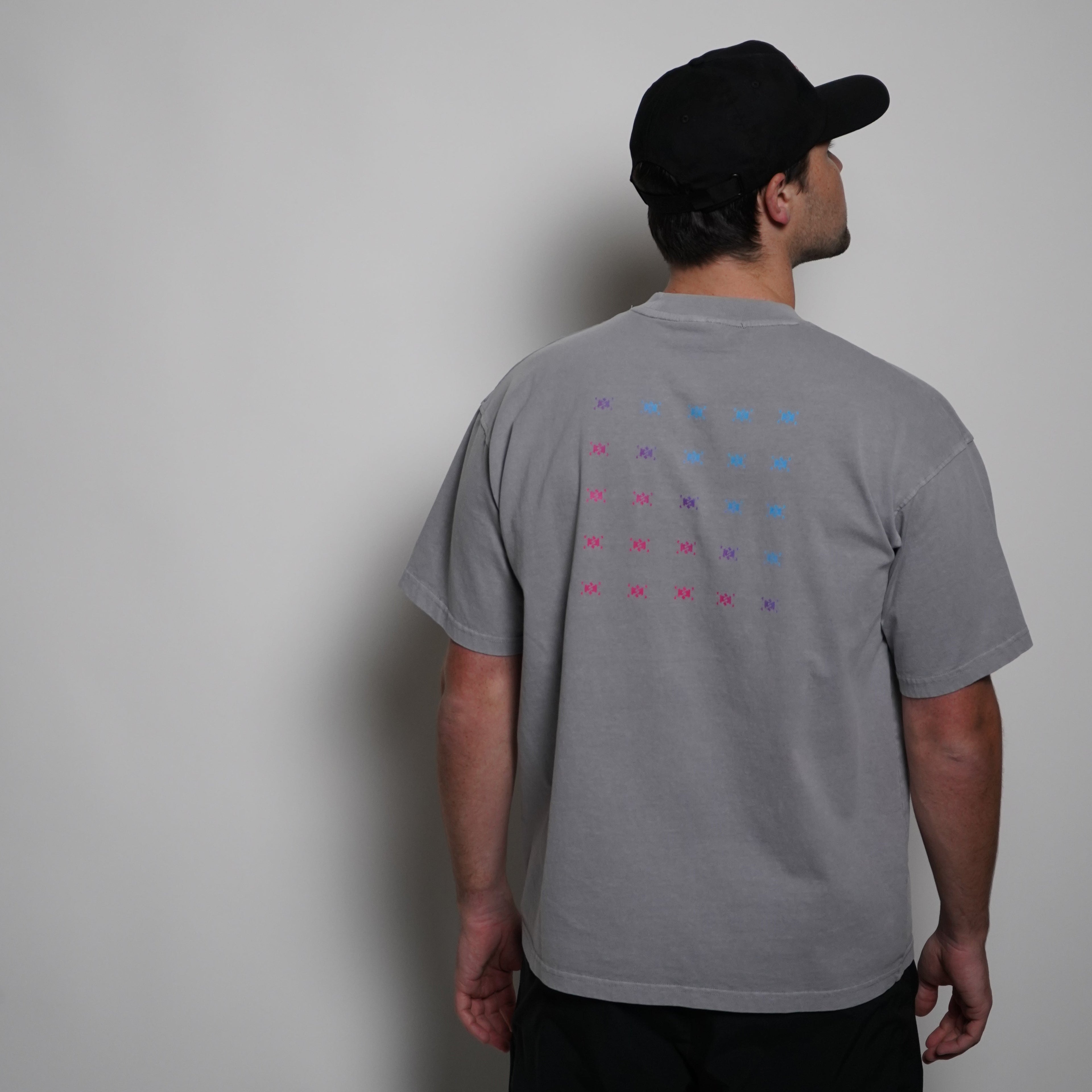 Person wearing a gray t-shirt with colorful pattern and black cap on a plain background