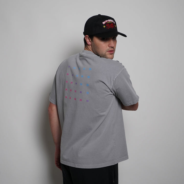 Person wearing a gray t-shirt with colorful patterns and a black cap on a plain background