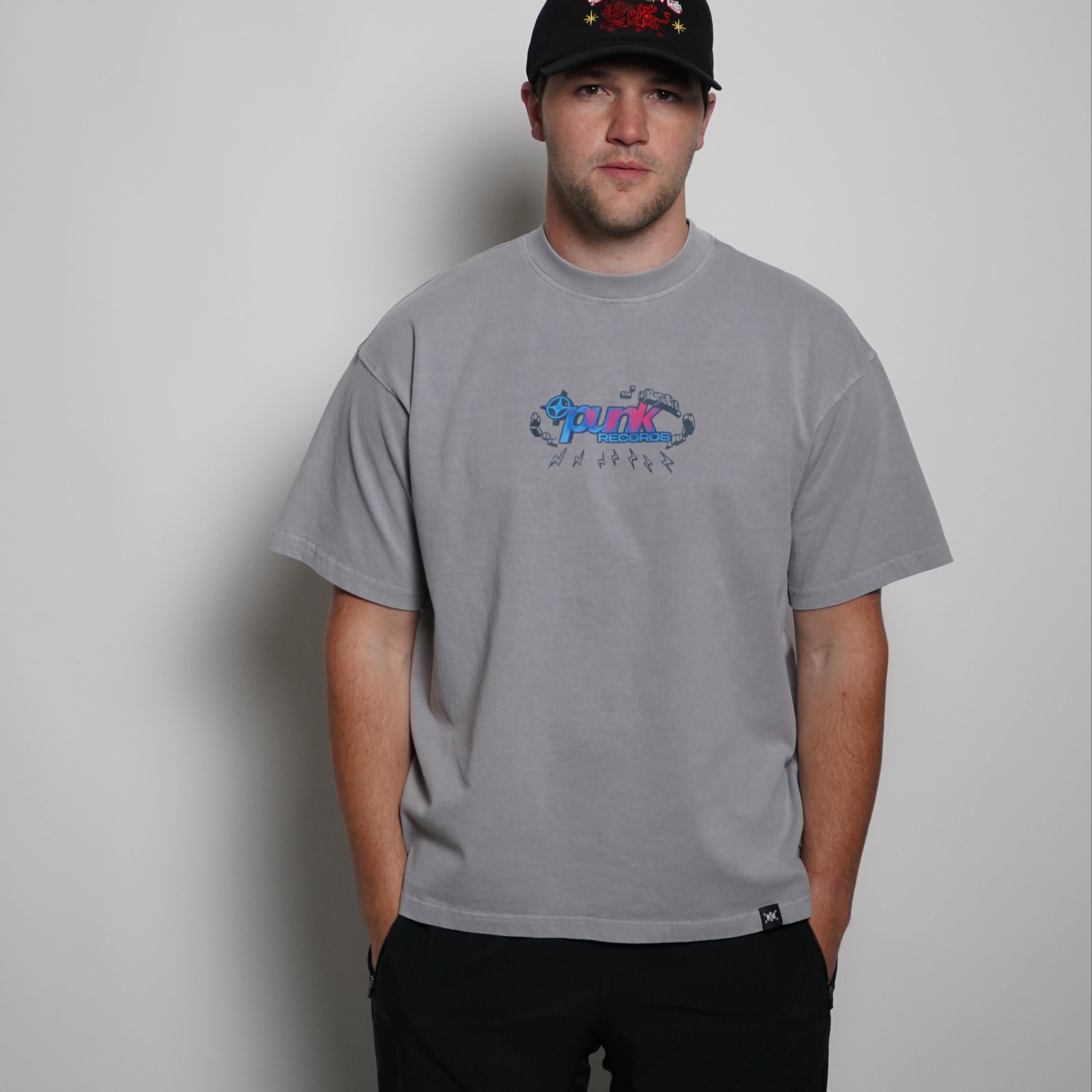 Person wearing a gray t-shirt with a logo and a black cap on a plain background