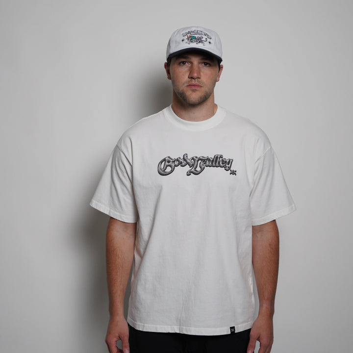 Person wearing a white t-shirt with text and a cap on a plain background