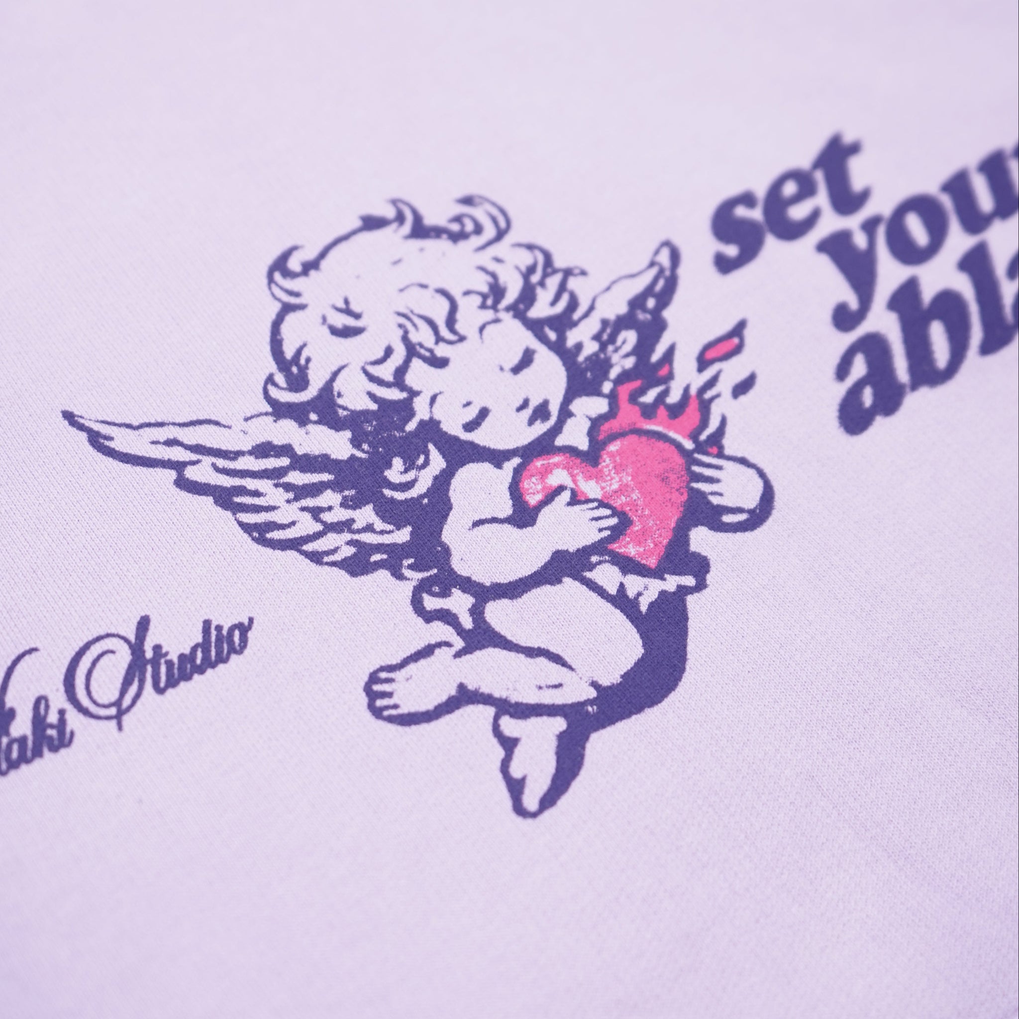 White sweatshirt with angel graphic and text on a light purple background