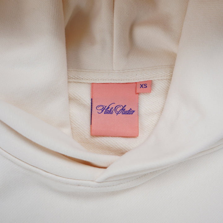 Close-up of a beige garment with a pink tag featuring the brand 'Folli Follie'.