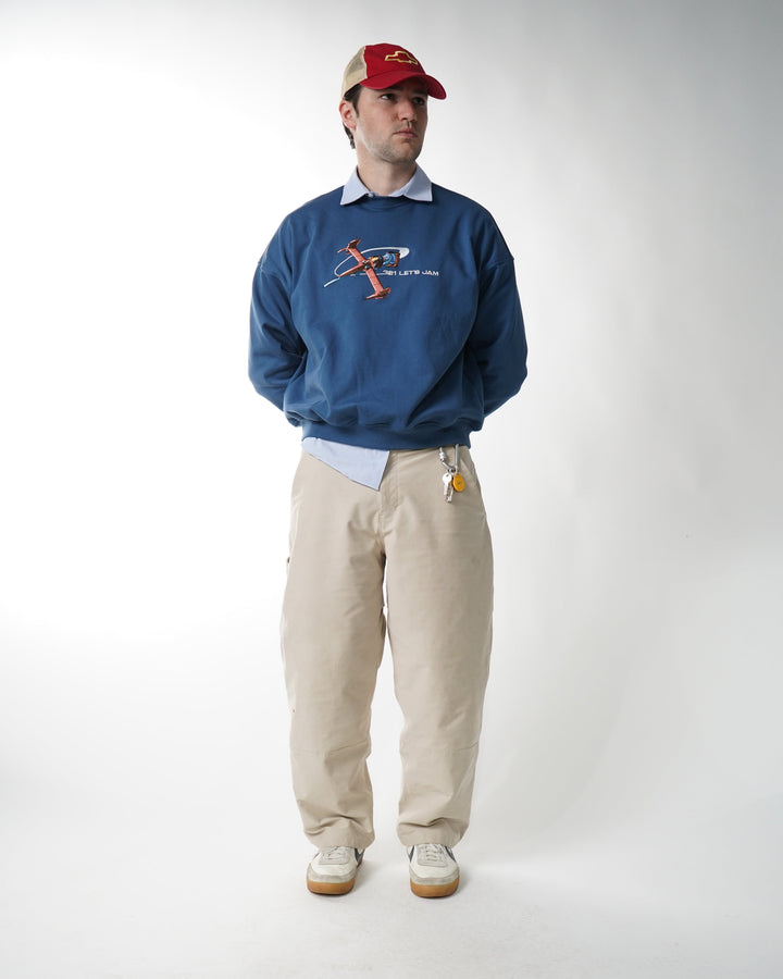 Man wearing a blue sweatshirt with a logo, beige pants, and a red cap on a white background