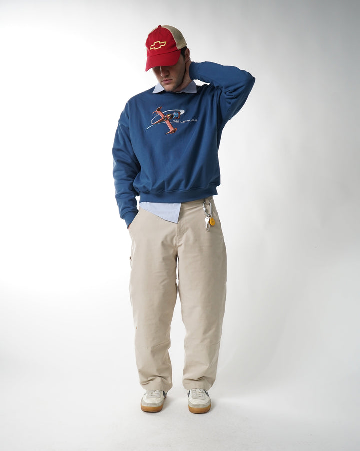 Person wearing a blue sweatshirt and beige pants on a white background