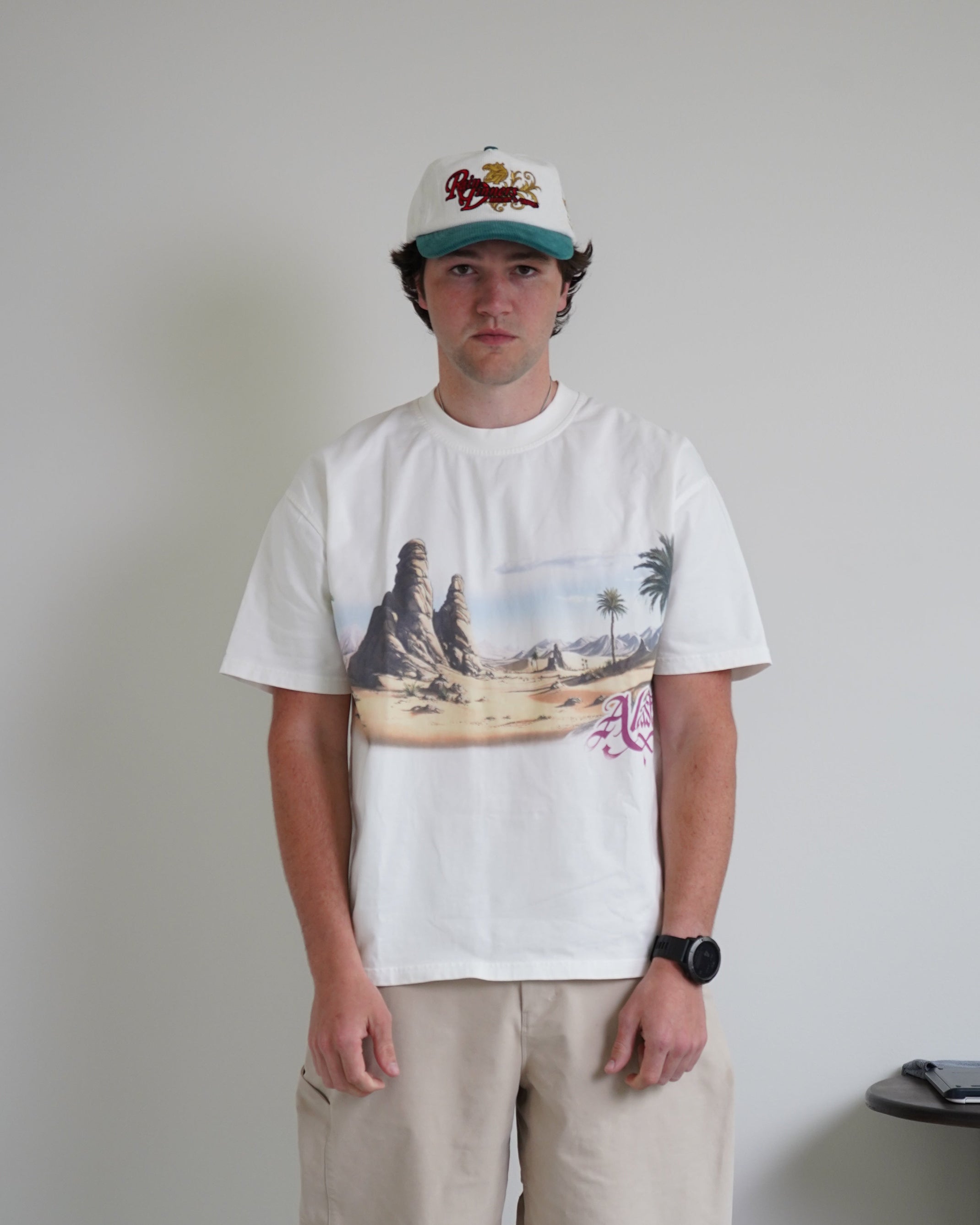 Person wearing a white t-shirt with a graphic design and beige pants standing on a tiled floor.